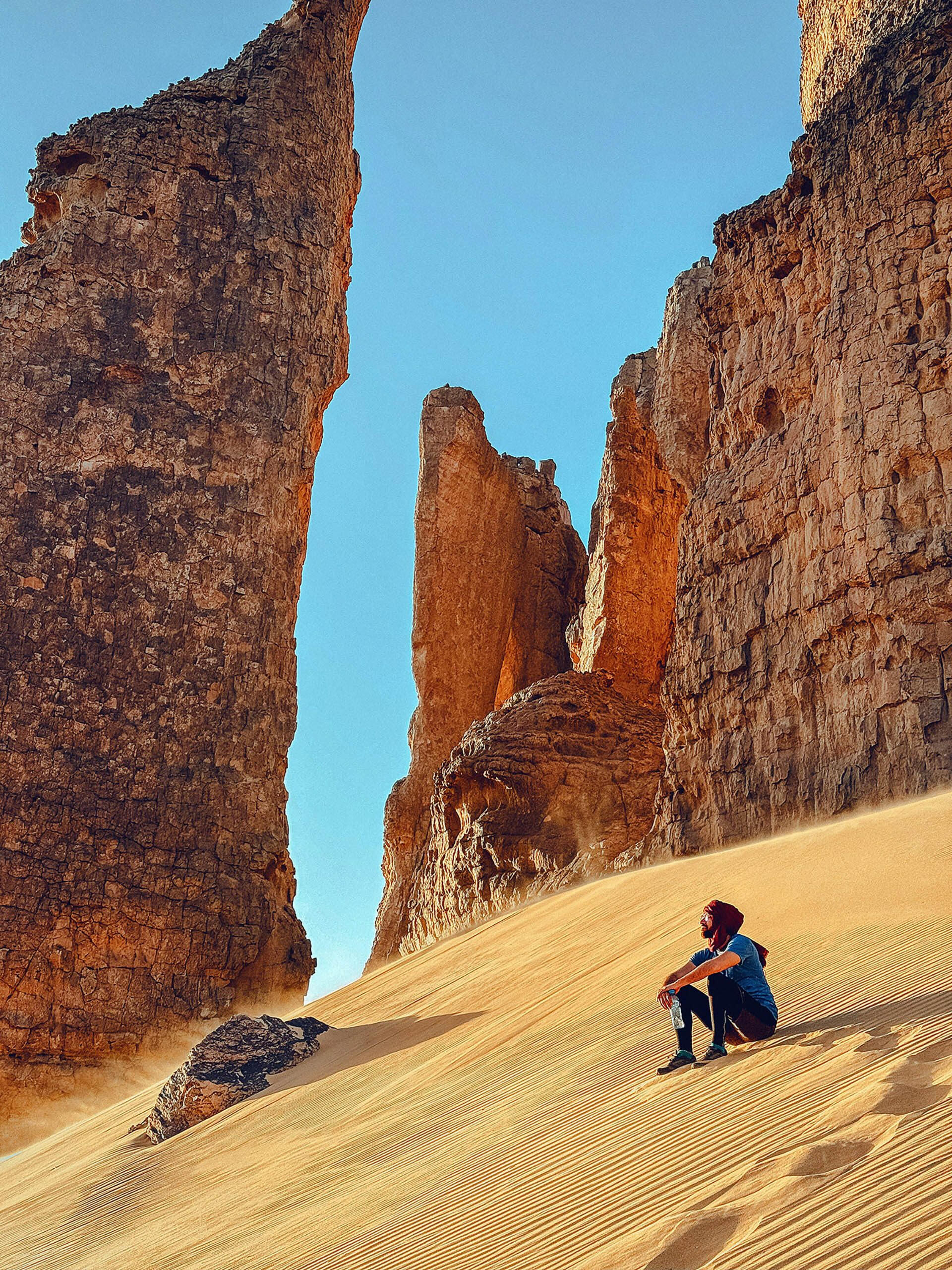 Traveller seated on golden sand at the foot of vast desert formations, evoking stillness, scale, and the immersive nature of Terra Noma’s remote travel design
