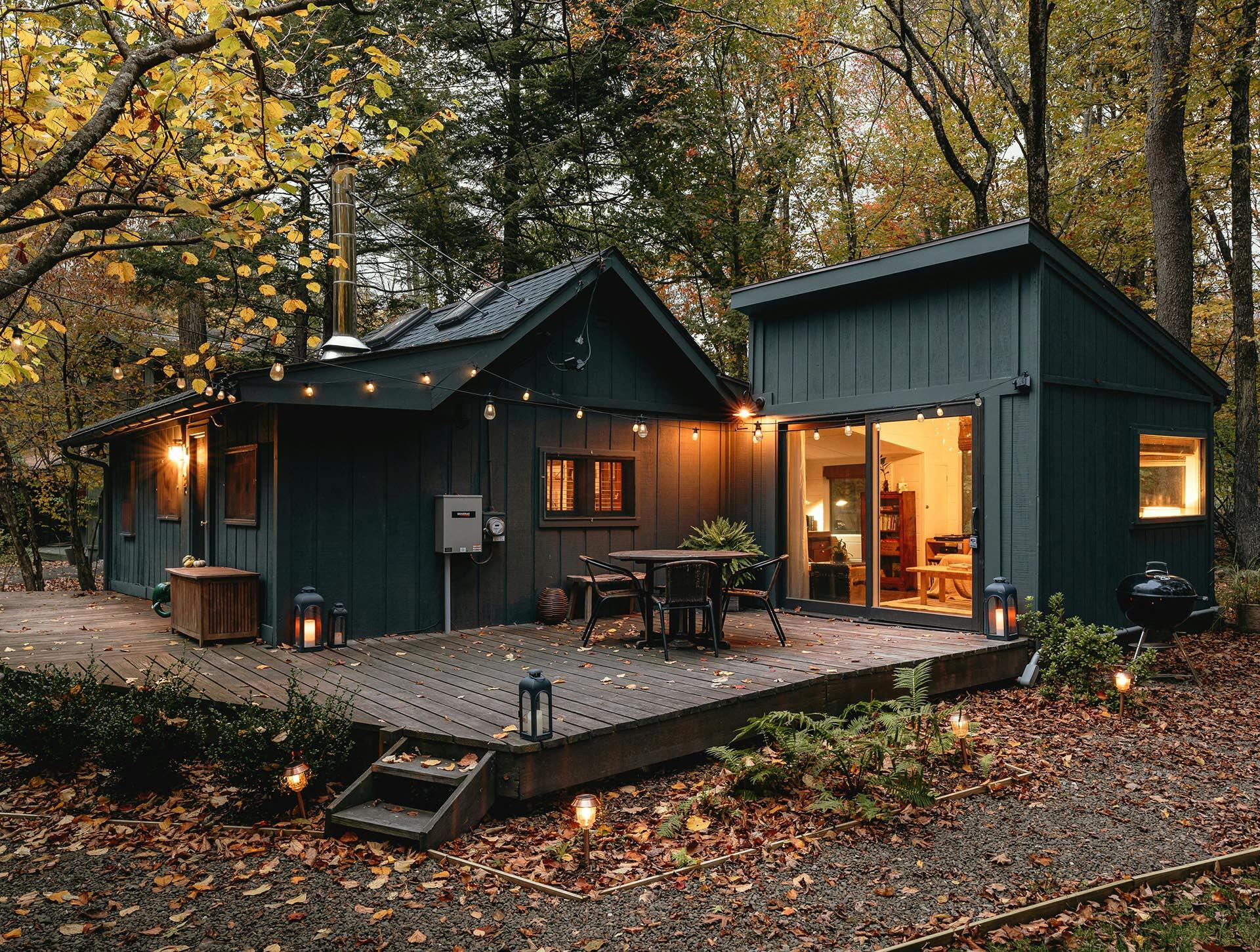 Modern cabin with a warm, open interior and outdoor deck surrounded by trees in autumn, reflecting Terra Noma’s approach to designing extended stays for creative work, clarity and quiet structure in naturally inspiring settings.